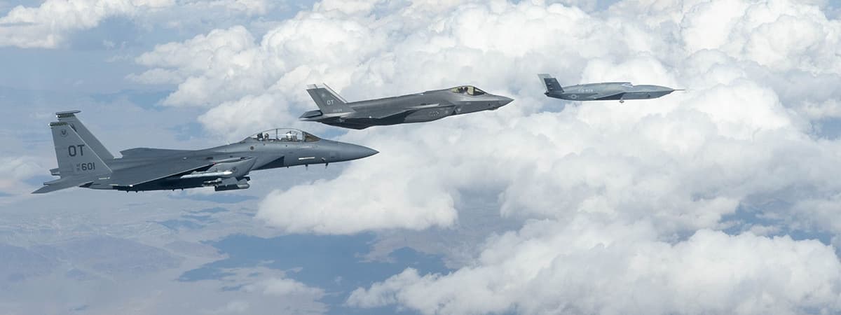 A General Atomics FQ-42 Vengeance  CCA  (right) flies in formation with a USAF F-35A and F-15E strike fighter.