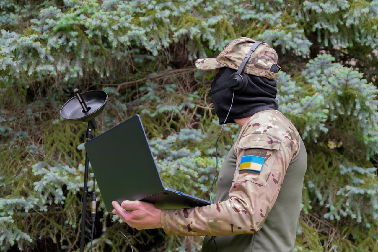 A Ukrainian soldier uses a directional microphone and a laptop in the forest, conducting radio reconnaissance.